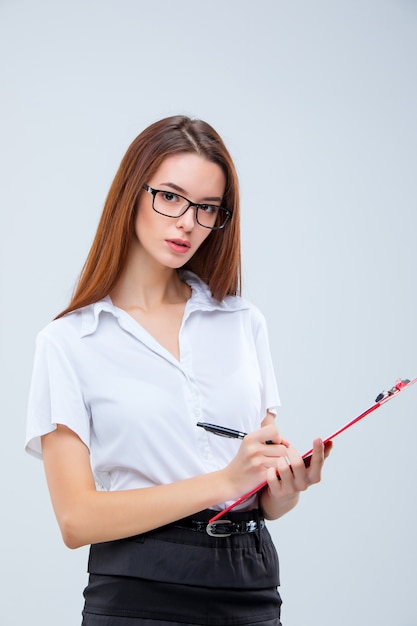 Молодая деловая женщина с ручкой и планшетом для заметок на серой стене