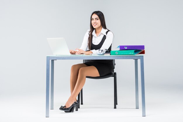 作業テーブルで若いビジネス女性は灰色で隔離のラップトップで動作します