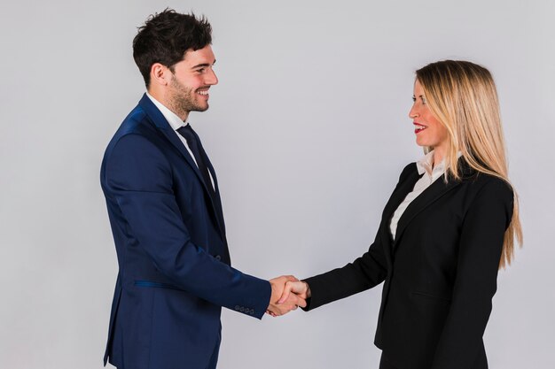 Young businessman and businesswoman shaking each other's hand against grey backdrop