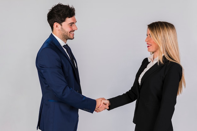 Young businessman and businesswoman shaking each other's hand against grey backdrop