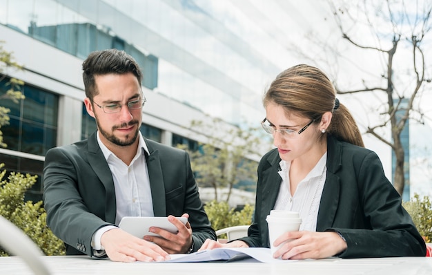 Free photo young businessman and businesswoman sitting at outdoor caf� looking at document