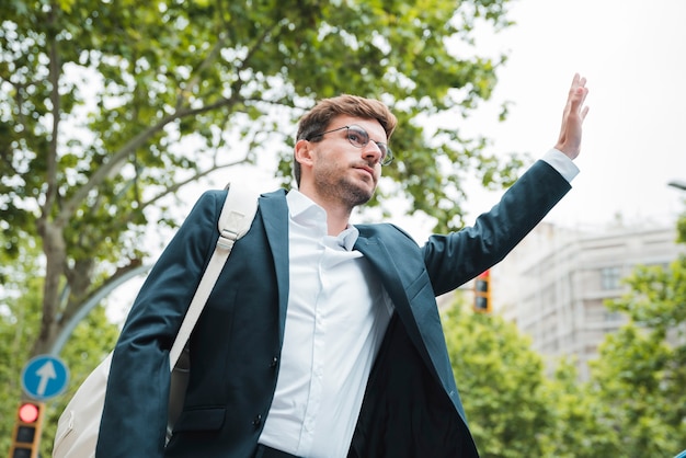Young businessman carrying white backpack on his shoulder hitchhiking