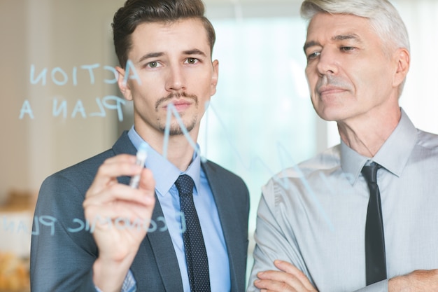 Young Businessman Drawing Graph Controlled by Boss