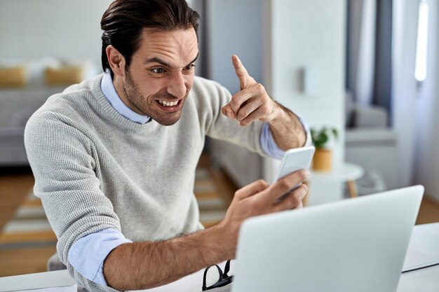 Young businessman feeling frustrated while reading text message on mobile phone at home