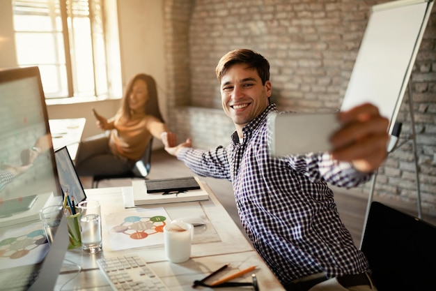 Young businessman and his colleague taking selfie with smart phone and having fun in the office