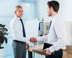 Free photo young businessman holding diary in hand shaking hands with his colleague