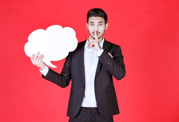 Young businessman holding empty speech bubble for advertisement