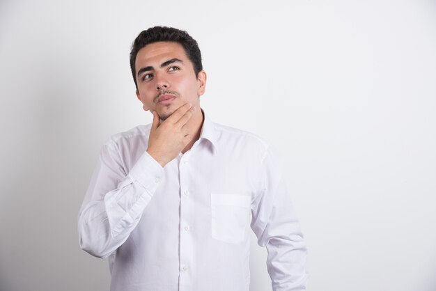 Young businessman holding his chin on white background.