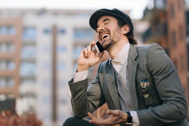 Young businessman laughing while talking to someone over cell phone on the street