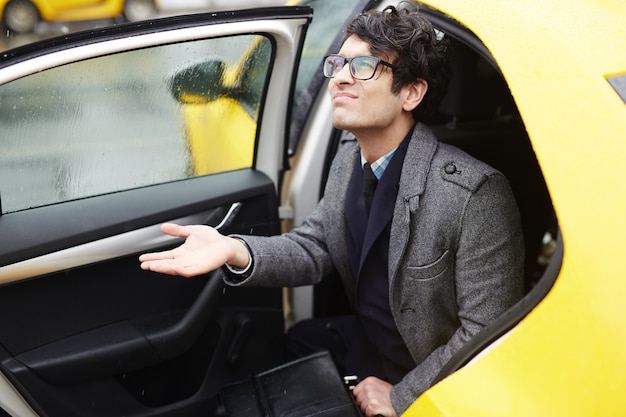 Free photo young businessman leaving taxi in rain