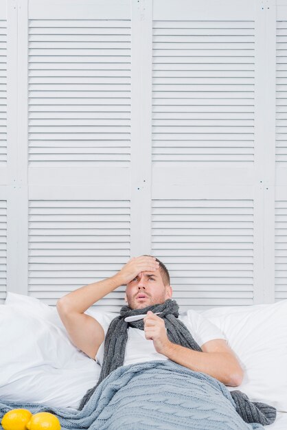 A young businessman lying on bed checking the forehead temperature with his hand