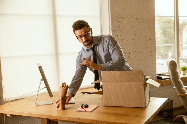 A young businessman moving in the office, getting new work place. Young caucasian male office worker equips new cabinet after promotion. Looks happy
