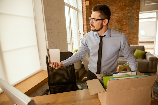 A young businessman moving in the office, getting new work place. Young caucasian male office worker equips new cabinet after promotion