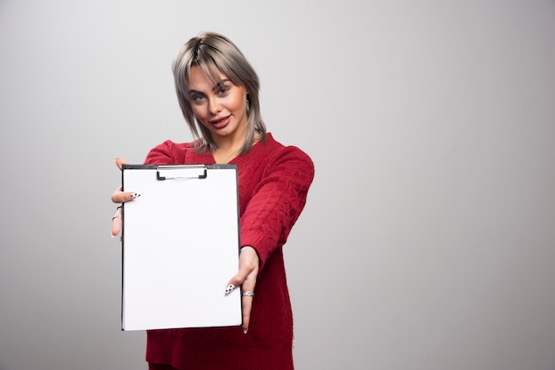 Young businessman showing clipboard on gray background.