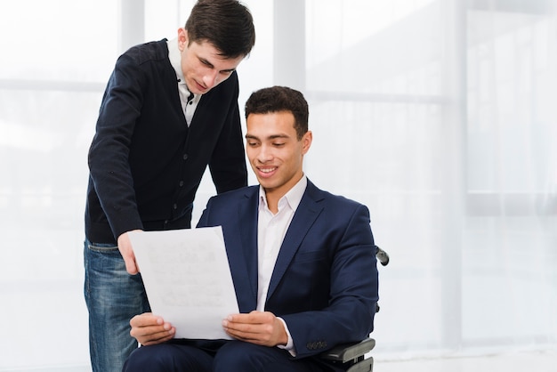 Free photo young businessman showing something on document to his colleague sitting on wheelchair