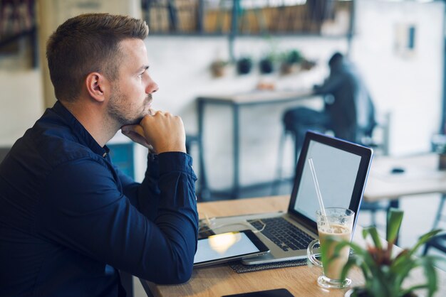 Young businessman sitting in cafe bar with laptop being worried and thinking about solution for his problem