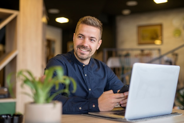 Free photo young businessman sitting in cozy cafe bar using laptop computer and looking aside