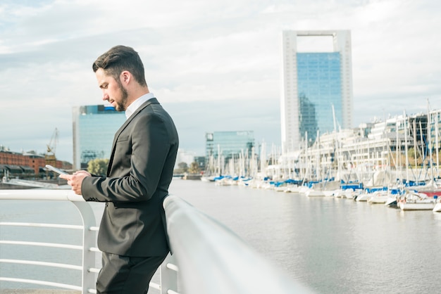 Young businessman standing near the railing using mobile phone