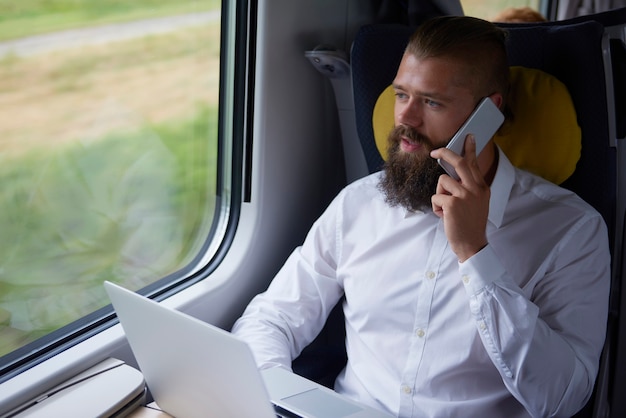Молодой бизнесмен разговаривает по мобильному телефону в поезде