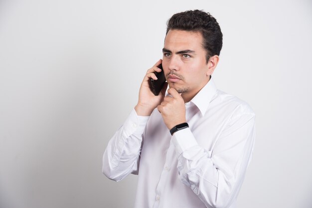 Молодой бизнесмен разговаривает с мобильным телефоном на белом фоне.