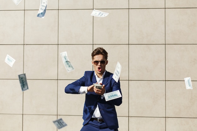 Free photo young businessman throughs around dollars and dances on the street