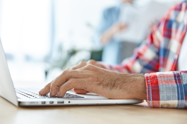 Young businessman uses modern laptop computer at office desk, types information, prepares financial report