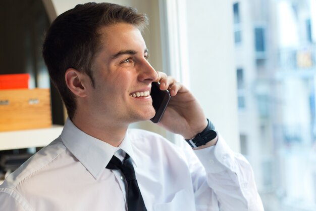 オフィスで彼の携帯電話を使用している若い実業家。
