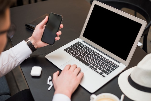 Young businessman using laptop looking at smartphone screen