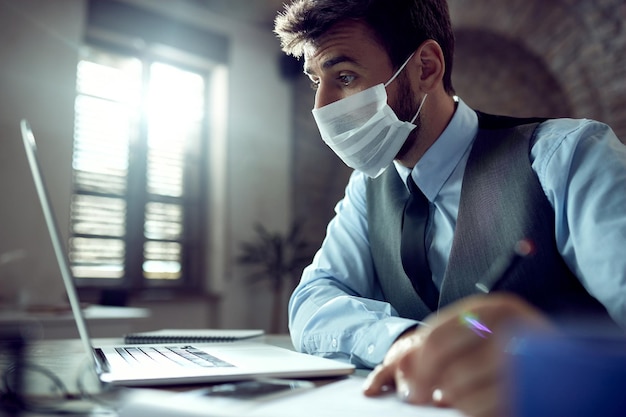 Young businessman wearing face mask while using laptop and working in the office during virus epidemic