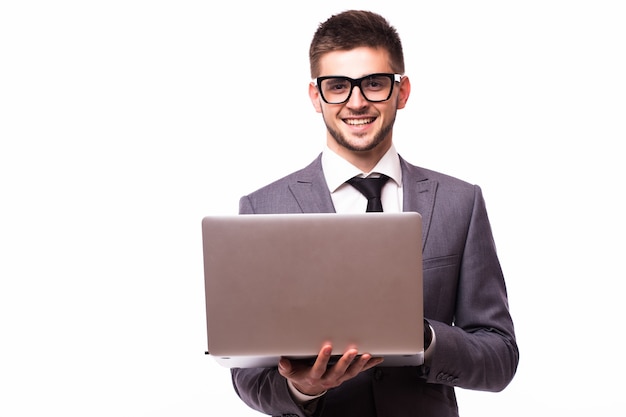 Молодой бизнесмен в очках работает с ноутбуком, стоя на белом фоне с уверенным выражением лица на умном лице, серьезно думая