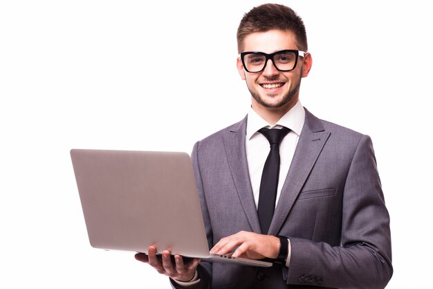 안경을 쓴 젊은 사업가는 진지하게 생각하는 똑똑한 얼굴에 자신감 있는 표정으로 배경 위에 서 있는 노트북을 사용하여 작업합니다.