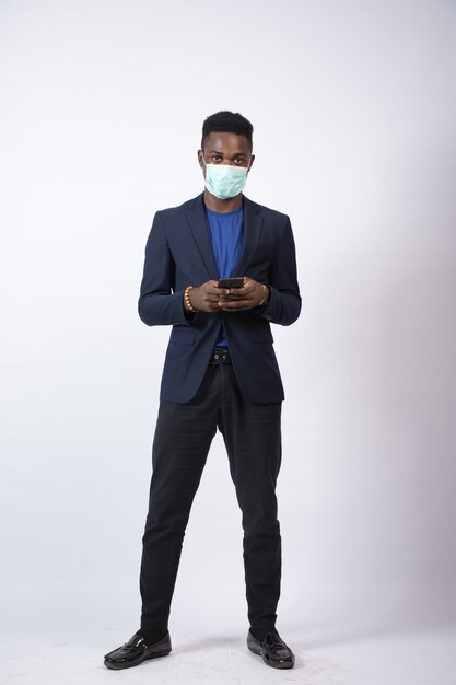 彼の携帯電話を使用してスーツとフェイスマスクを身に着けている青年実業家