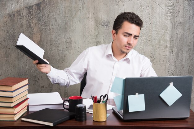 Young businessman with book looking at laptop at the desk.