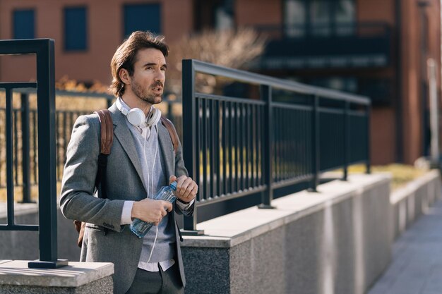 Young businessman with bottle of water walking in the city