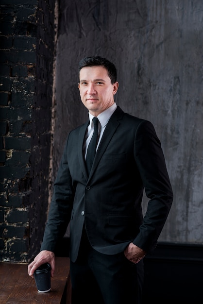 Young businessman with coffee cup and hand in pocket looking at camera