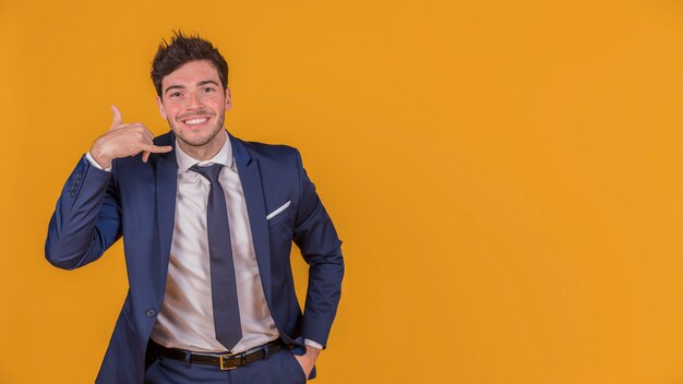 Young businessman with hand in his pocket making call gesture against an orange backdrop