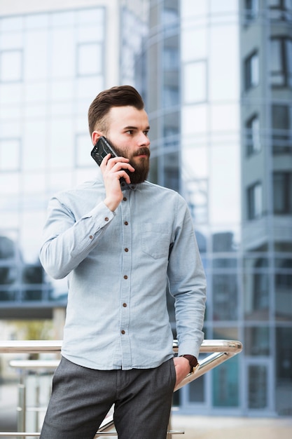 Young businessman with hands in his pocket talking on mobile phone