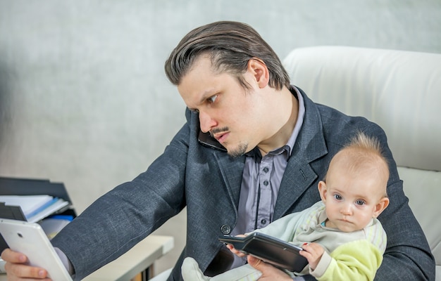 Free photo young businessman working from his office and holding a baby