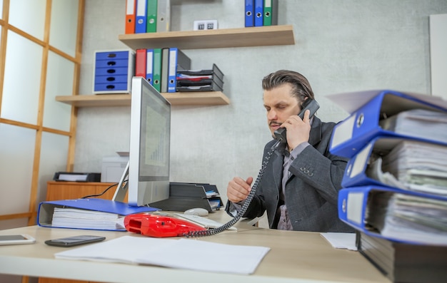 Giovane uomo d'affari che lavora dal suo ufficio mentre parla al telefono