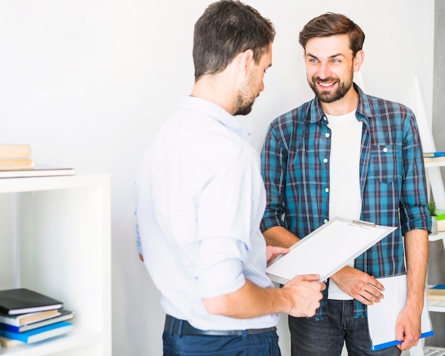 Young businessmen with folder and clipboard standing in office