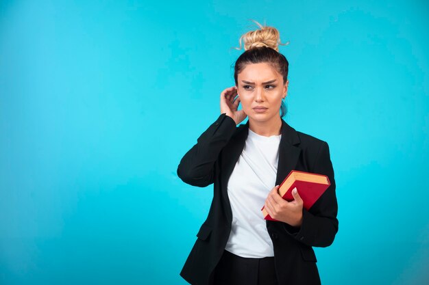 Young businesswoman in black blazer holding a book and trying to remember something.