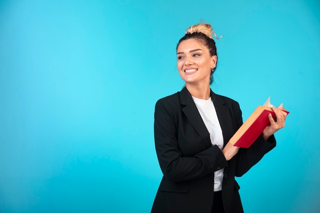 Free photo young businesswoman in black blazer holding a taskbook and reading it.