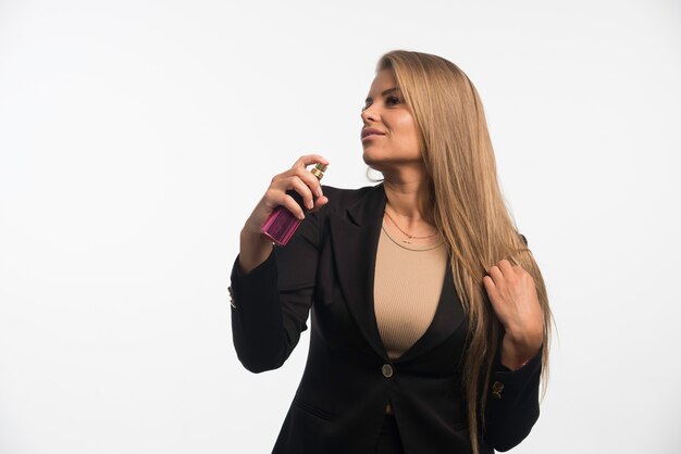 Young businesswoman in black suit applies perfume to her neck. 