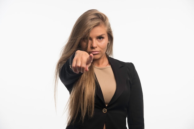 Young businesswoman in black suit pointing forward. 