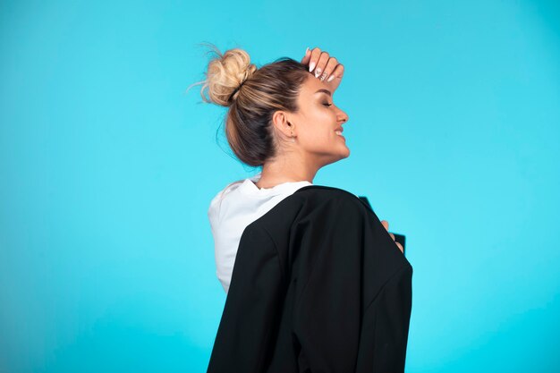 Young businesswoman in bun holding a black blazer and looks confident.