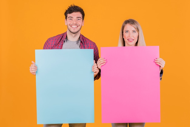 Young businesswoman and businessman holding blue and pink placard against an orange background