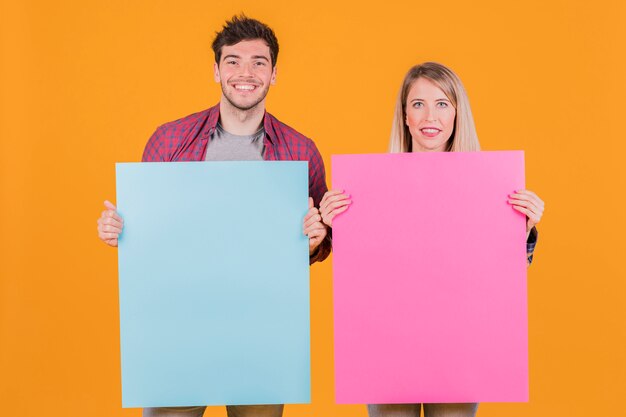 Young businesswoman and businessman holding blue and pink placard against an orange background