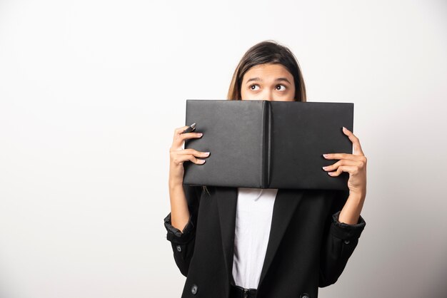Young businesswoman covering her face with an opened clipboard . 