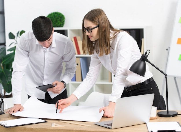 Young businesswoman discussing project with her male colleague on white paper over the desk