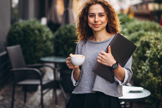 ラップトップを保持しているカフェの外でコーヒーを飲む若い実業家